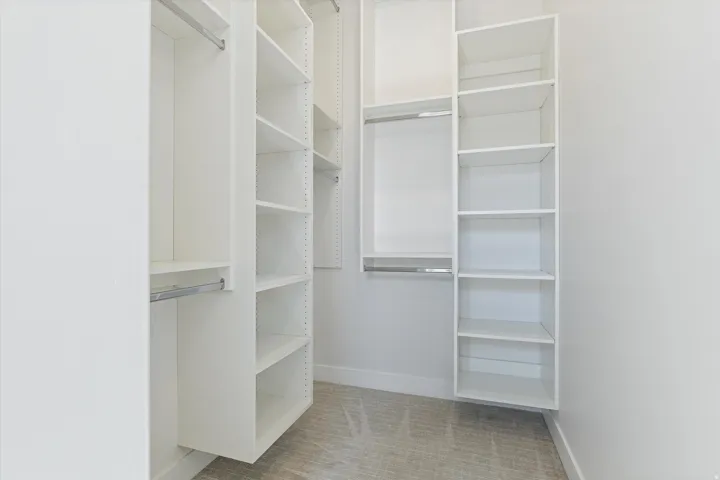 Walk-in closet featuring white built-in shelving, chrome hanging rods, and light-colored carpet flooring