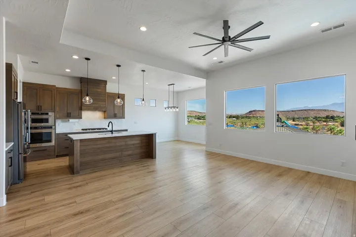 Open-concept living space featuring wood-finish flooring, a modern kitchen with built-in stainless steel appliances, a large center island with a white countertop, and expansive windows showcasing a distant mountainous landscape