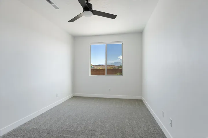 Bright room with a large window, gray carpet, and a ceiling fan
