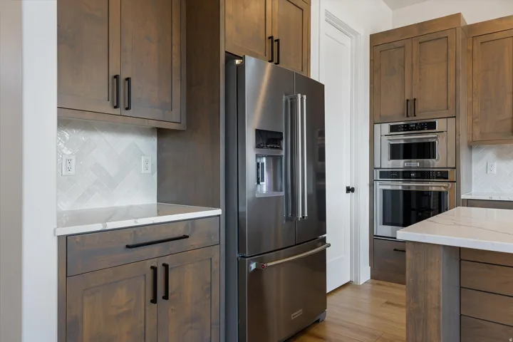 Kitchen featuring wood-finish cabinetry, stainless steel appliances, white quartz countertops, and a white herringbone tile backsplash