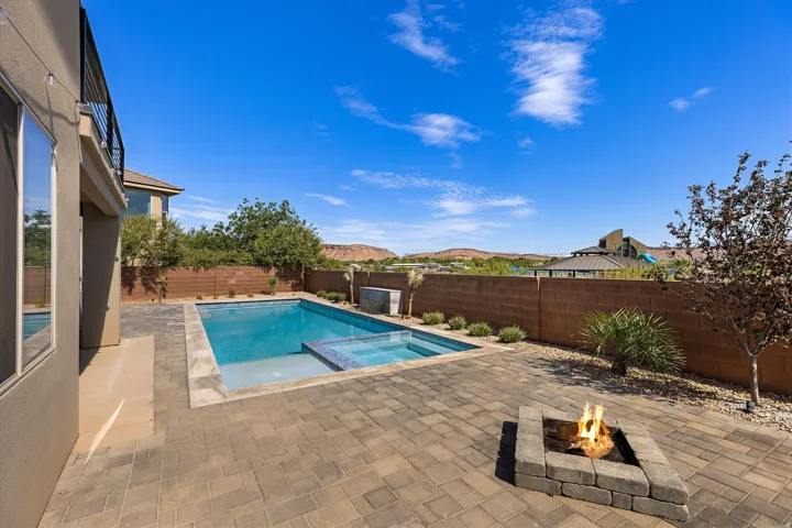 Expansive paver patio featuring a swimming pool with integrated spa and a stone fire pit