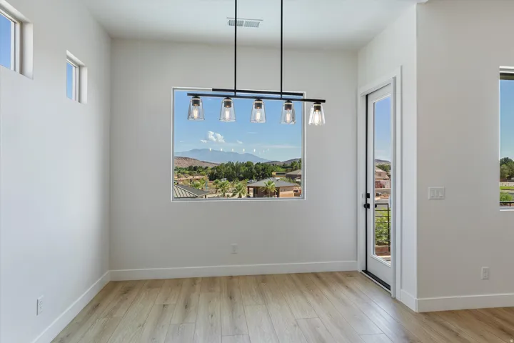 Spacious room featuring wood-finish flooring, a contemporary linear chandelier with four glass shades, and multiple windows