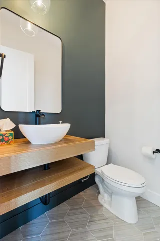 Modern powder room featuring a floating wood-finish vanity with an integrated shelf, a white vessel sink, and a matte black faucet