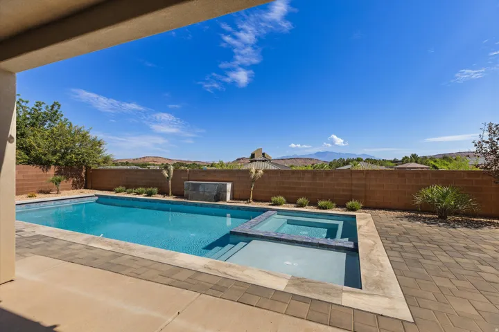 Outdoor living area featuring a rectangular swimming pool with an integrated spa, paver decking, and a low-maintenance landscape