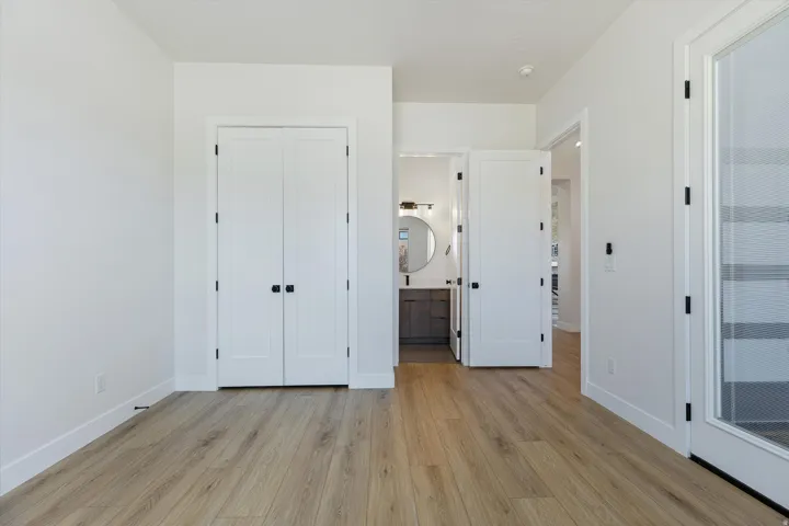 Light wood-finish flooring extending through an open doorway, white baseboards, and white walls