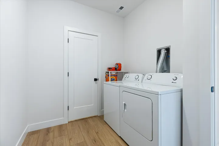 Dedicated laundry area featuring wood-finish flooring, white walls, and a contemporary white door with matte black hardware