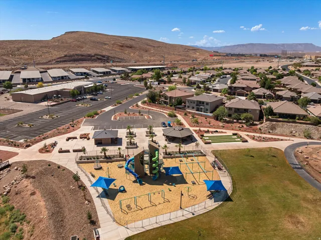Community park featuring a spacious playground with multiple structures, shaded seating areas, a large grassy expanse, and a paved walking path