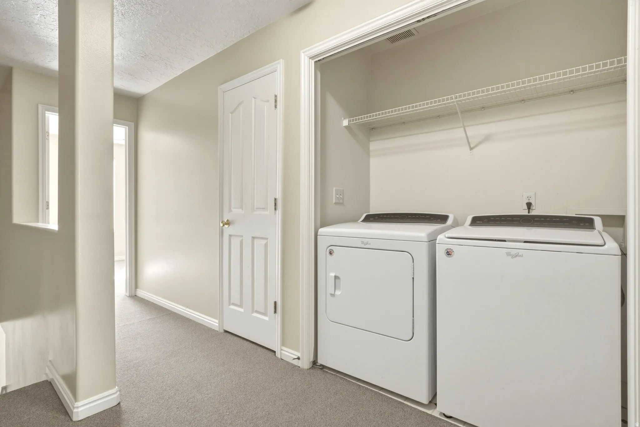 Convenient laundry area featuring a white washer and dryer, wire shelving, and neutral carpeting