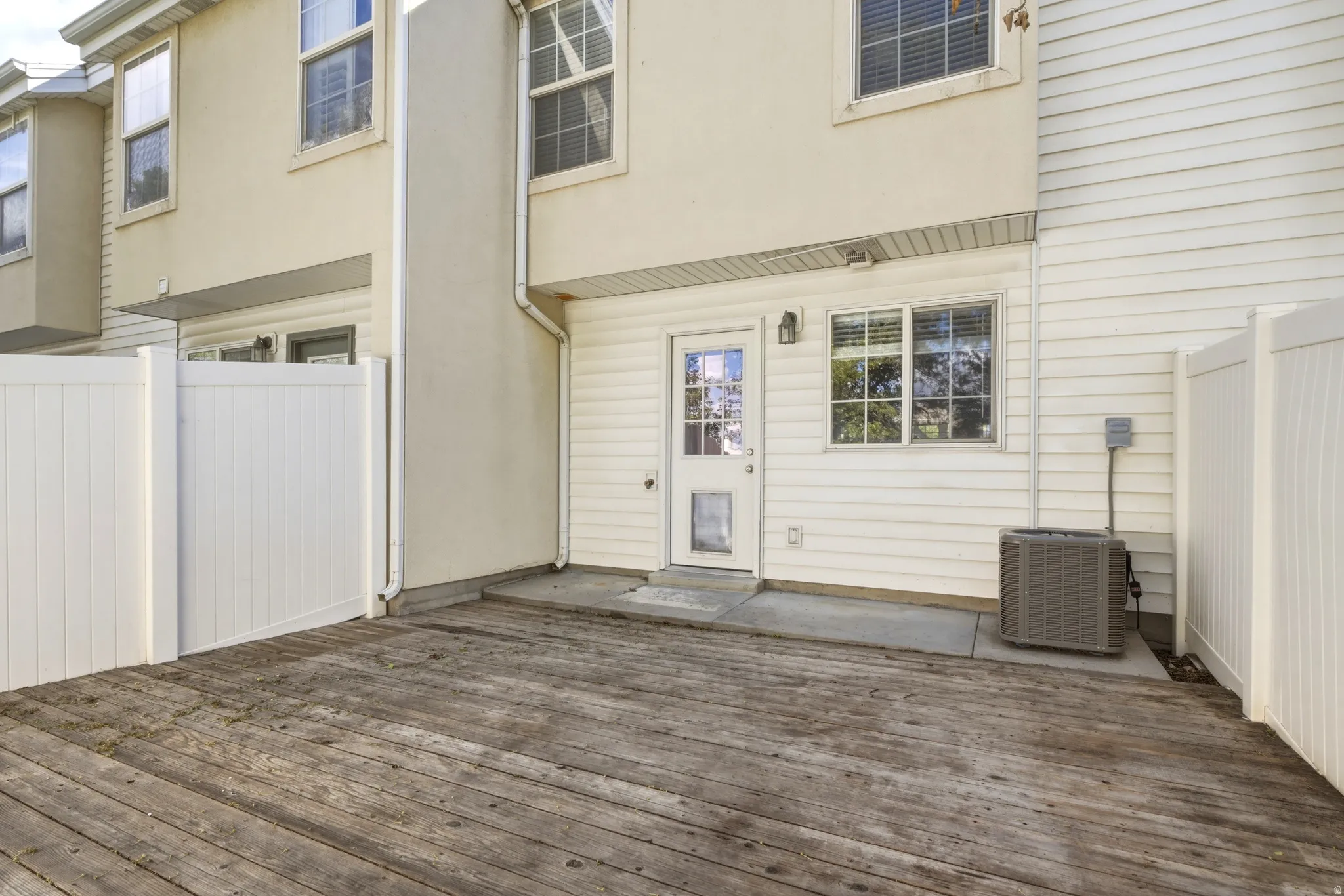 Private outdoor deck area featuring a full vinyl privacy fence, a glass-paneled exterior door, and an exterior wall light fixture