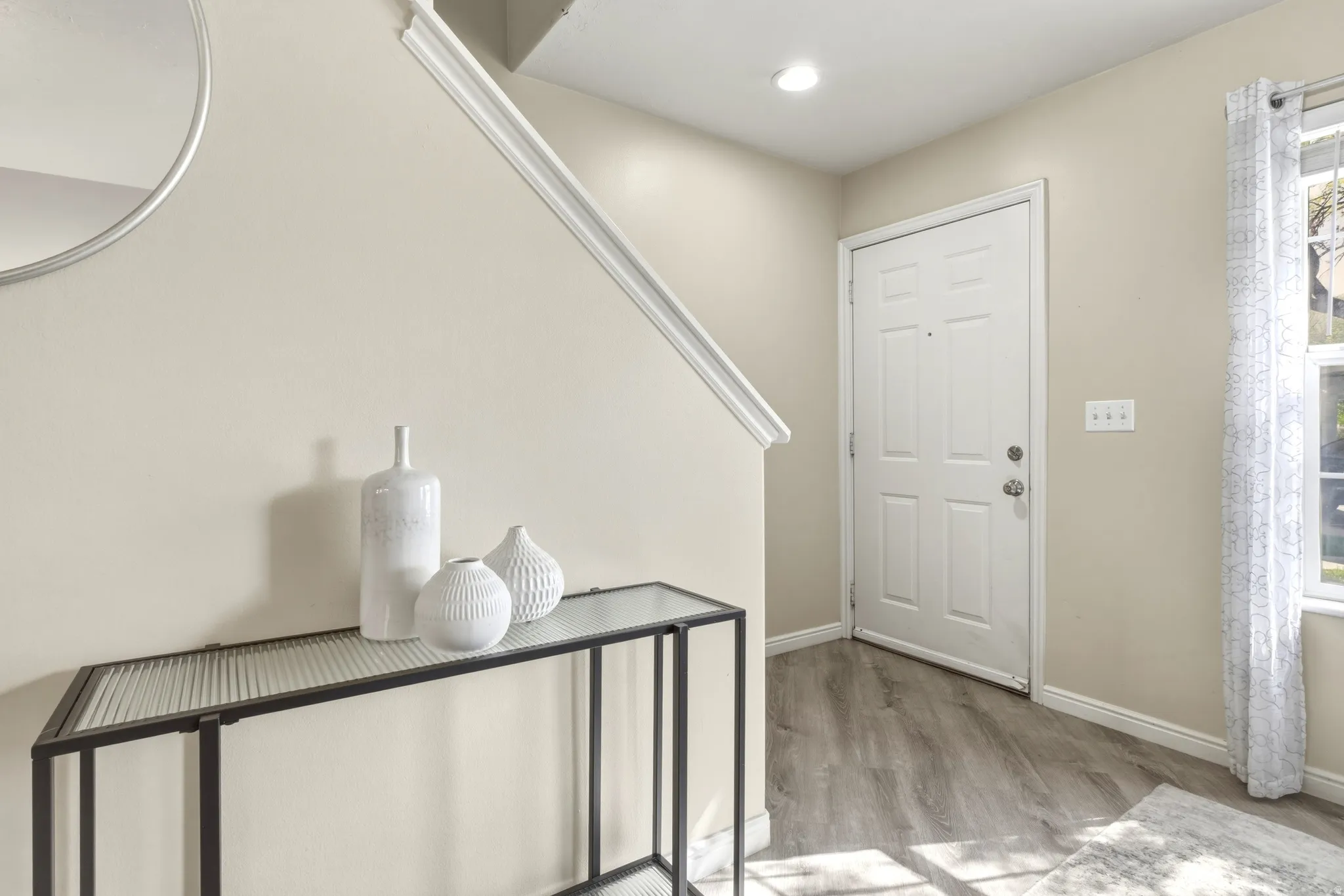 Entryway featuring wood-finish flooring, a white paneled door, and a staircase with white trim