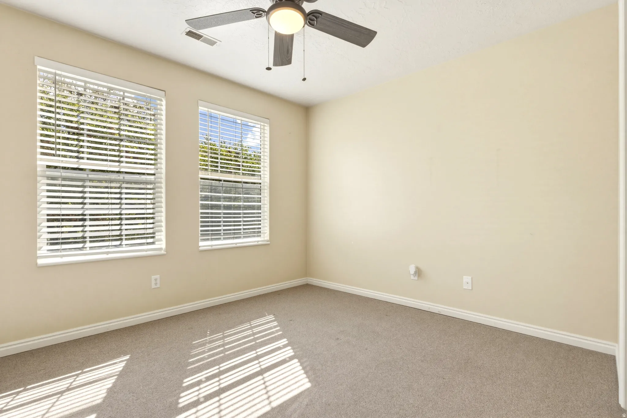 Room featuring two windows with horizontal blinds, neutral carpet flooring, and a ceiling fan with integrated lighting