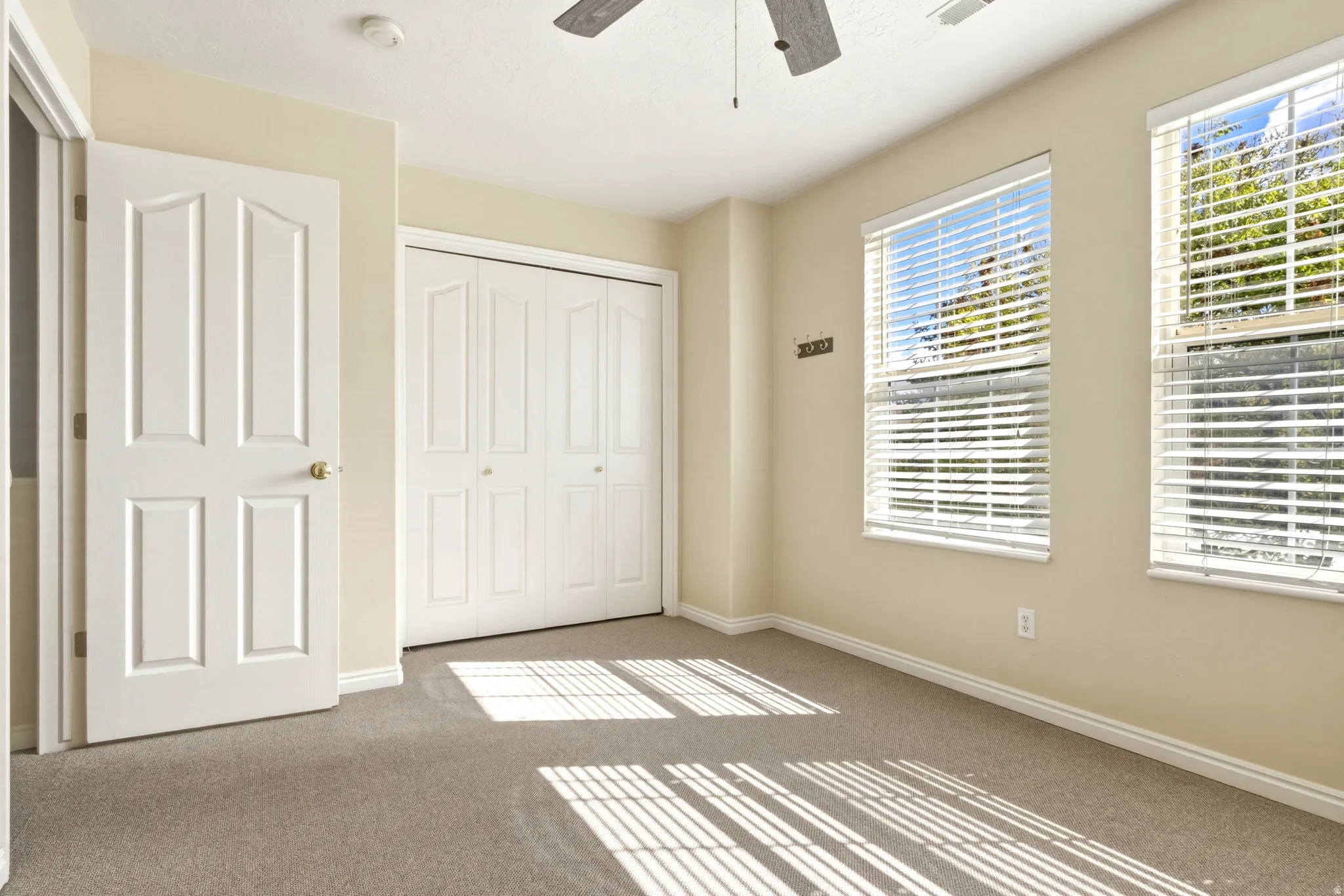 Carpeted room featuring dual windows with blinds, a ceiling fan, a paneled door, and bi-fold closet doors