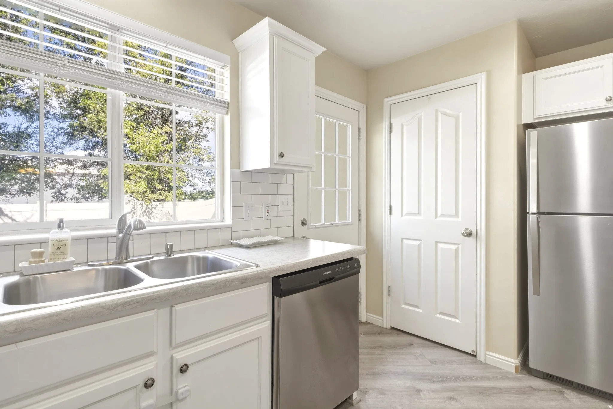Kitchen featuring white cabinetry, subway tile backsplash, stainless steel appliances, and wood-finish flooring