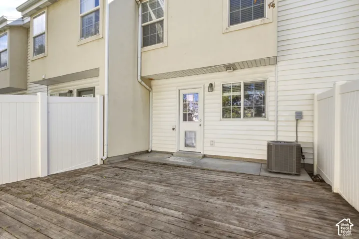 Private outdoor deck area featuring a full vinyl privacy fence, a glass-paneled exterior door, and an exterior wall light fixture