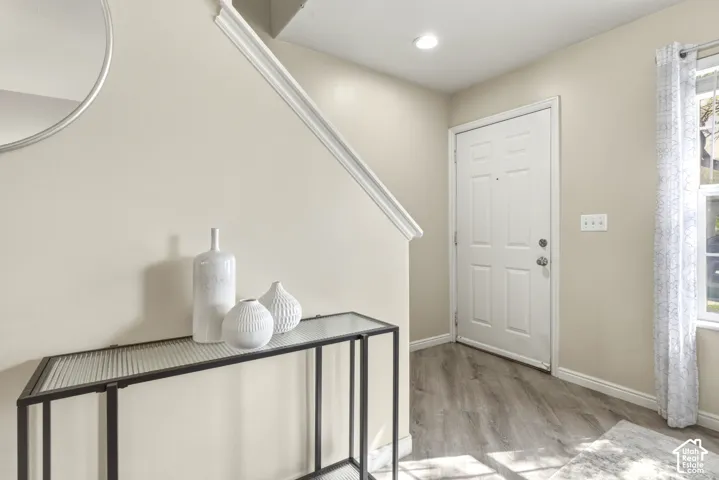 Entryway featuring wood-finish flooring, a white paneled door, and a staircase with white trim