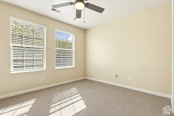 Room featuring two windows with horizontal blinds, neutral carpet flooring, and a ceiling fan with integrated lighting
