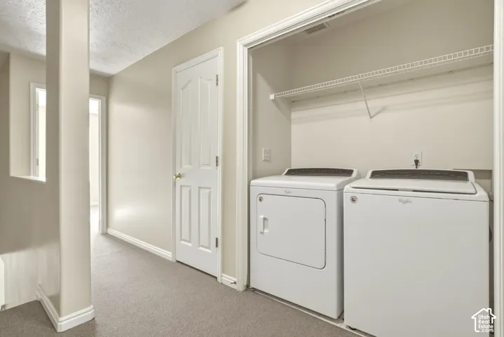 Convenient laundry area featuring a white washer and dryer, wire shelving, and neutral carpeting