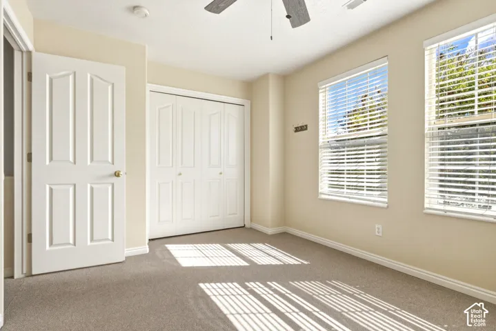Carpeted room featuring dual windows with blinds, a ceiling fan, a paneled door, and bi-fold closet doors