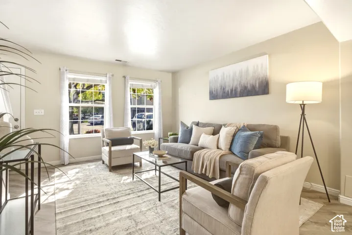 Spacious living area featuring light-toned wall paint and wood-finish flooring