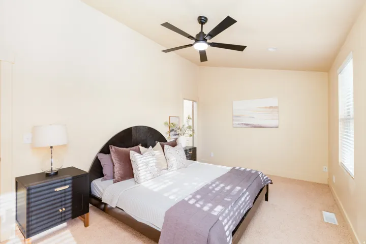 Spacious primary bedroom featuring vaulted ceilings, a contemporary ceiling fan with can lighting, and neutral wall tones. Three windows for lots of natural light.