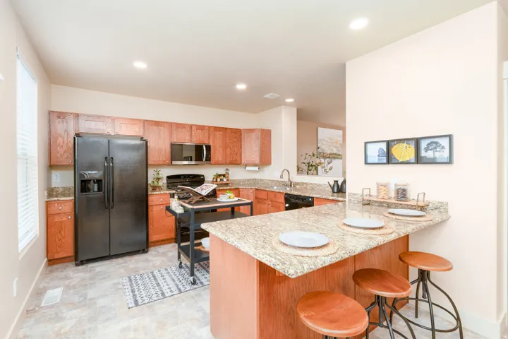 Kitchen featuring wood cabinetry, granite countertops, black appliances, and a breakfast bar.