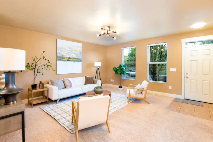 Carpeted living area featuring a neutral color palette, multiple windows with blinds, and a paneled entry door with lots of natural light.