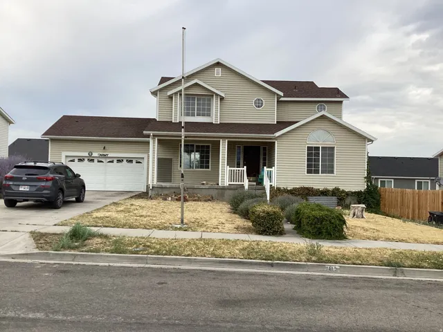 Two-story residence featuring light-colored siding, a covered front porch with white railings, an attached two-car garage, and a driveway
