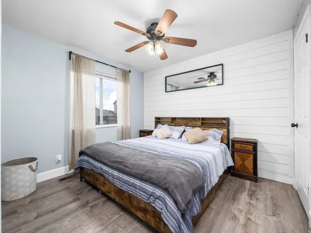 Bedroom featuring a prominent shiplap accent wall, wood-finish flooring, and a ceiling fan with integrated lighting
