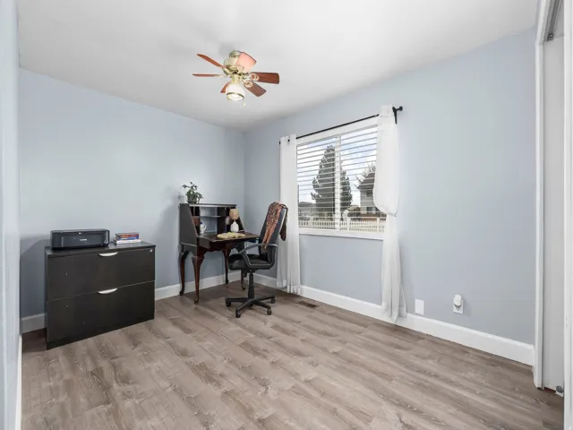 Spacious room featuring wood-finish flooring, light blue walls, and a large window with white blinds