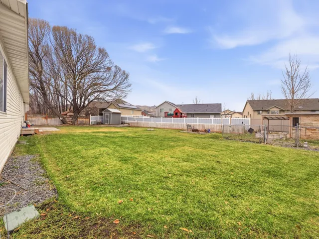Expansive green lawn featuring a white privacy fence, mature trees, a detached storage shed, and a raised garden bed