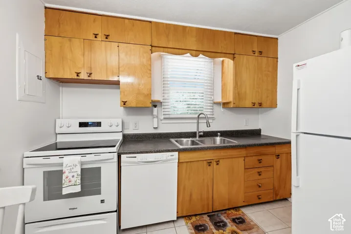 Kitchen featuring wood cabinetry, white appliances, a double basin stainless steel sink, and dark countertops