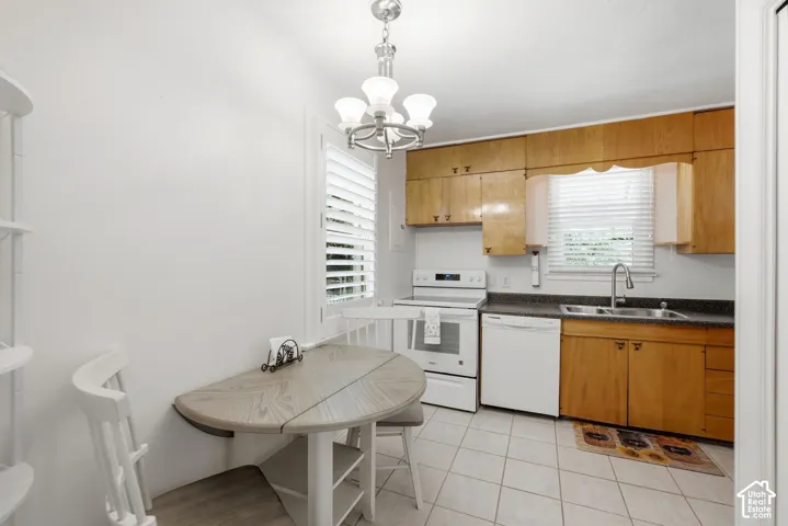 Kitchen featuring wood cabinetry, white appliances, a stainless steel sink, and light-toned tile flooring