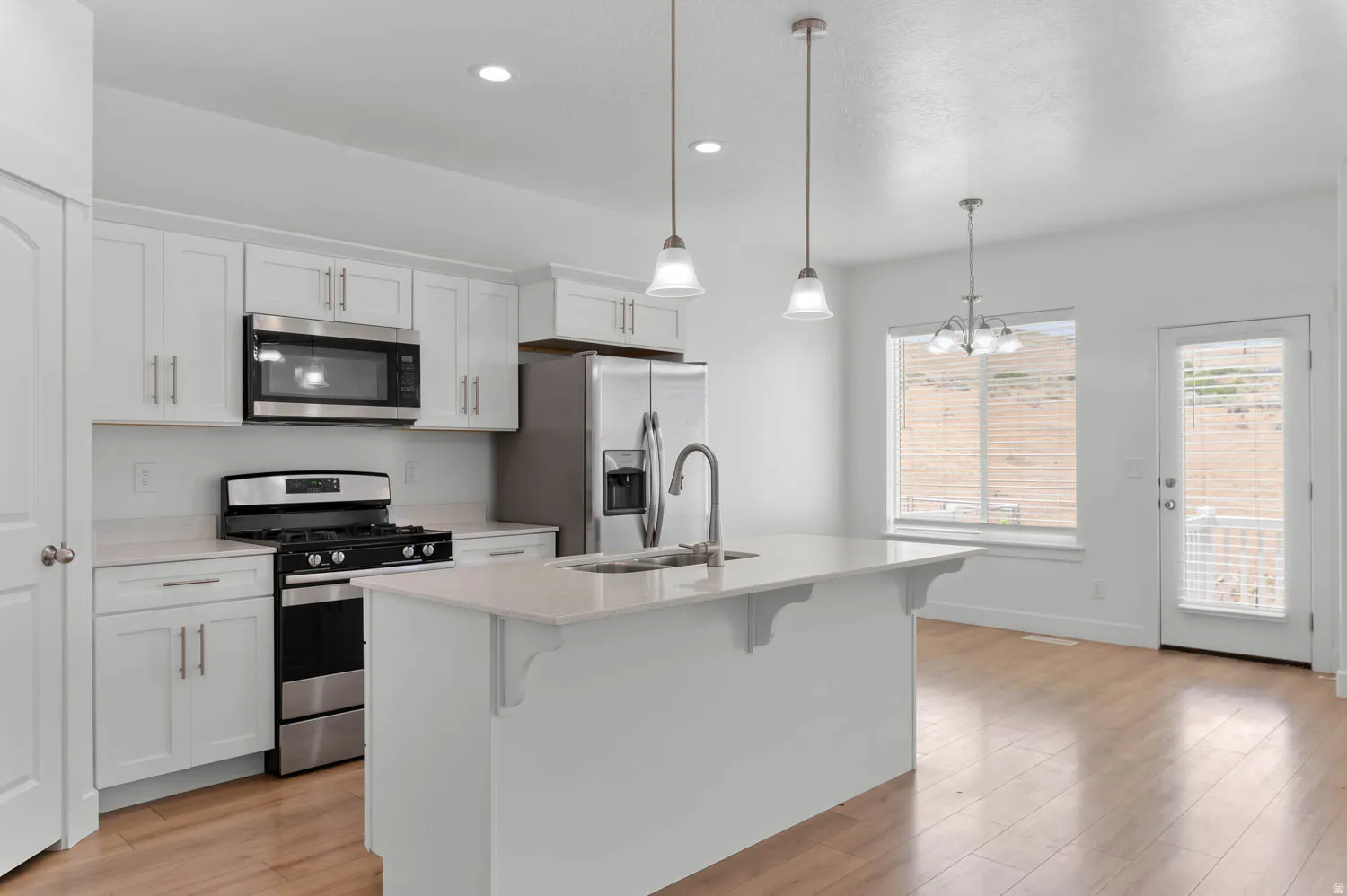 Modern kitchen featuring white cabinetry, stainless steel appliances, a center island with sink, pendant lighting, and wood-finish flooring