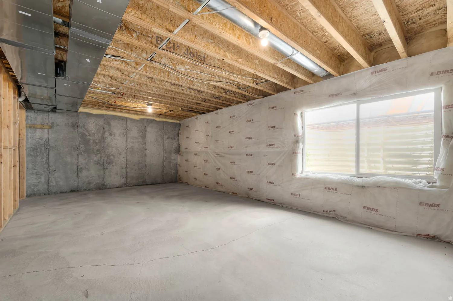 Unfinished lower level featuring exposed wood joists, concrete flooring, and a large window