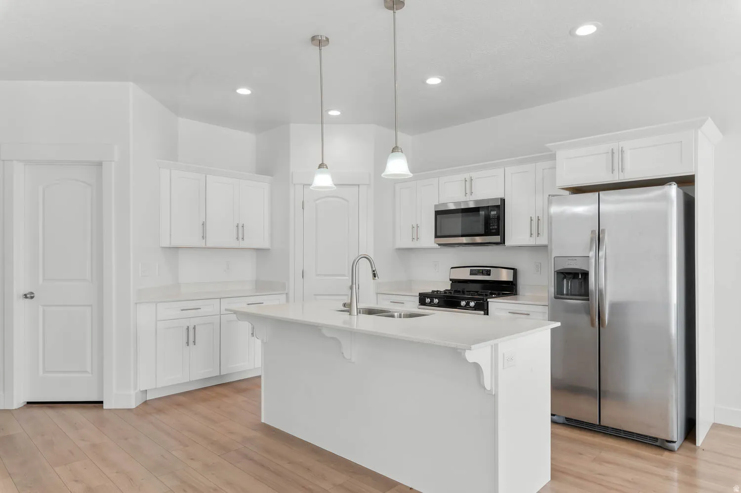 Open-concept kitchen featuring white cabinetry, light-toned countertops, and wood-finish flooring