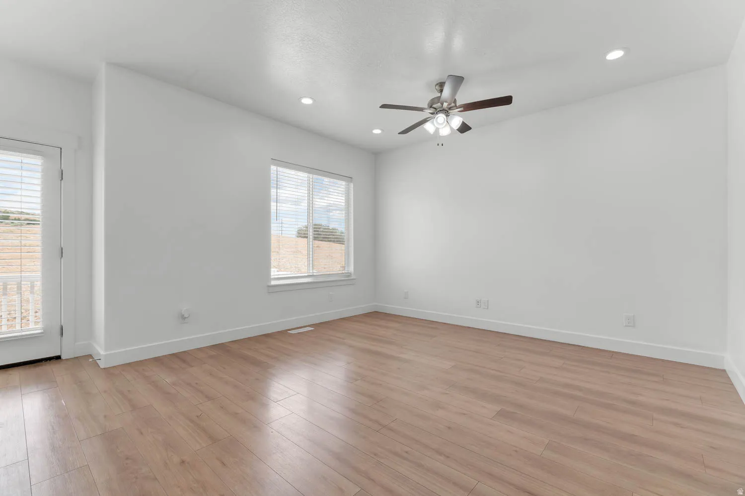 Spacious room featuring wood-finish flooring, a ceiling fan with integrated lighting, recessed lighting, and a window with blinds