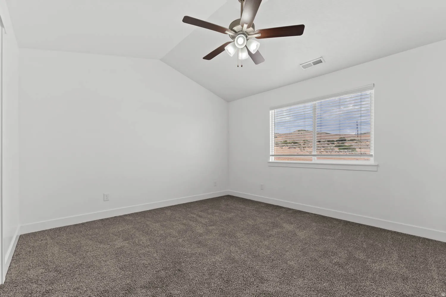 Bedroom featuring vaulted ceilings, neutral-toned carpeting, a ceiling fan with light fixture, and a window with horizontal blinds offering a distant landscape backdrop