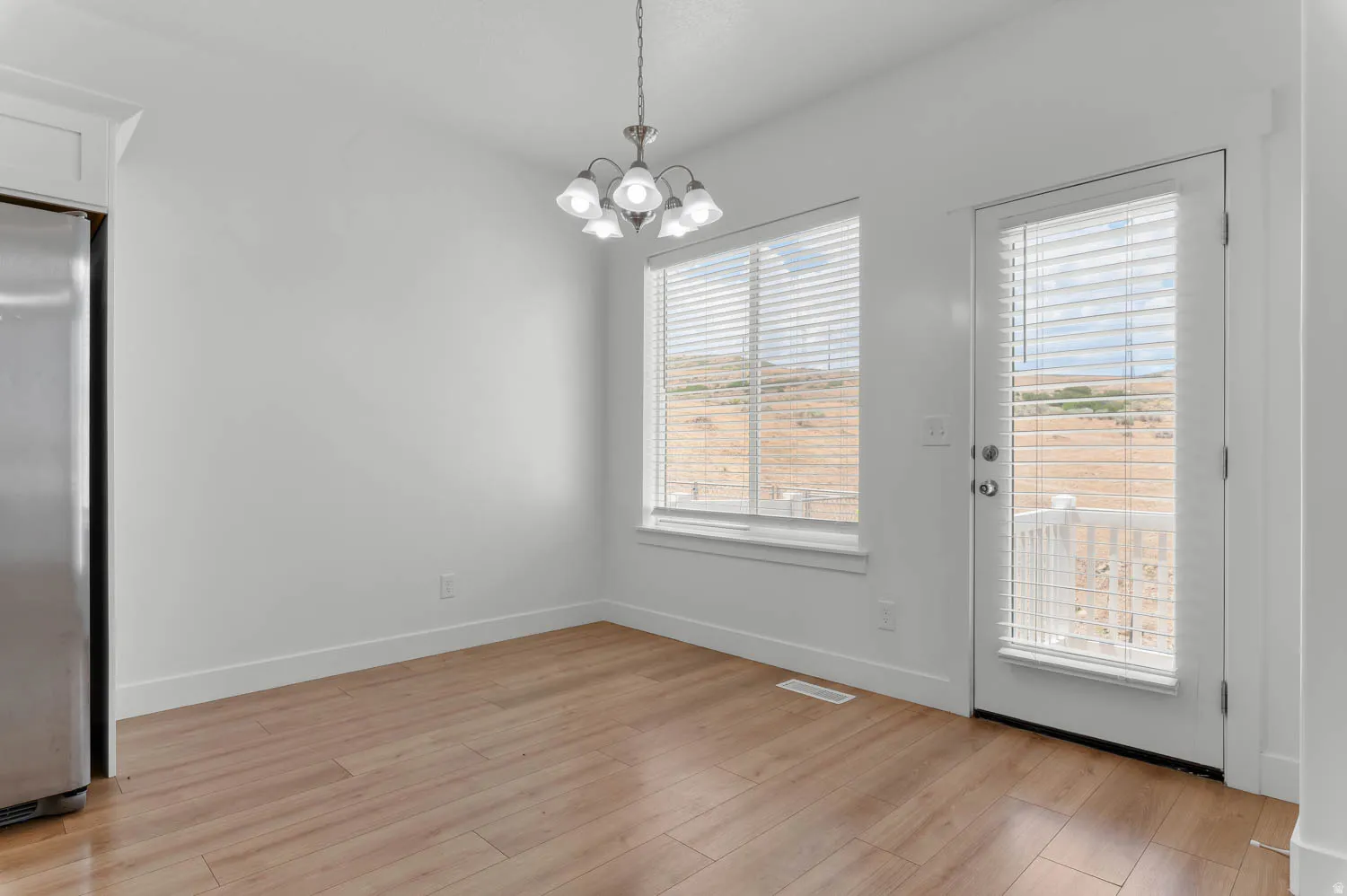 Open-concept dining area featuring wood-finish flooring, a contemporary chandelier, and a glass-paneled door with integrated blinds