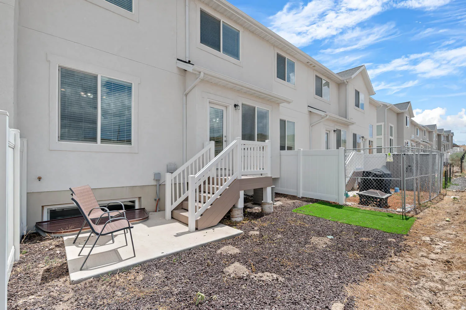 Rear exterior with a concrete patio, wood-finish deck, and white railing system