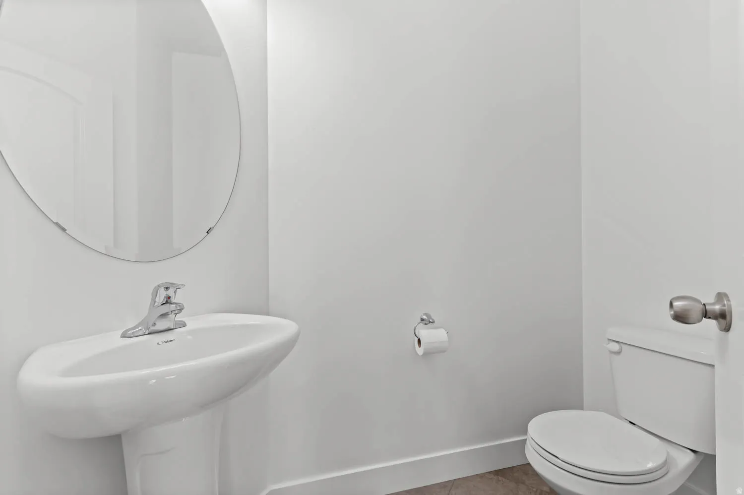 Pedestal sink with chrome faucet, circular frameless mirror, and a white toilet