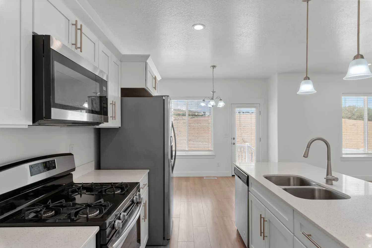 Modern kitchen featuring white cabinetry with gold-tone hardware, stainless steel appliances, and light-toned countertops