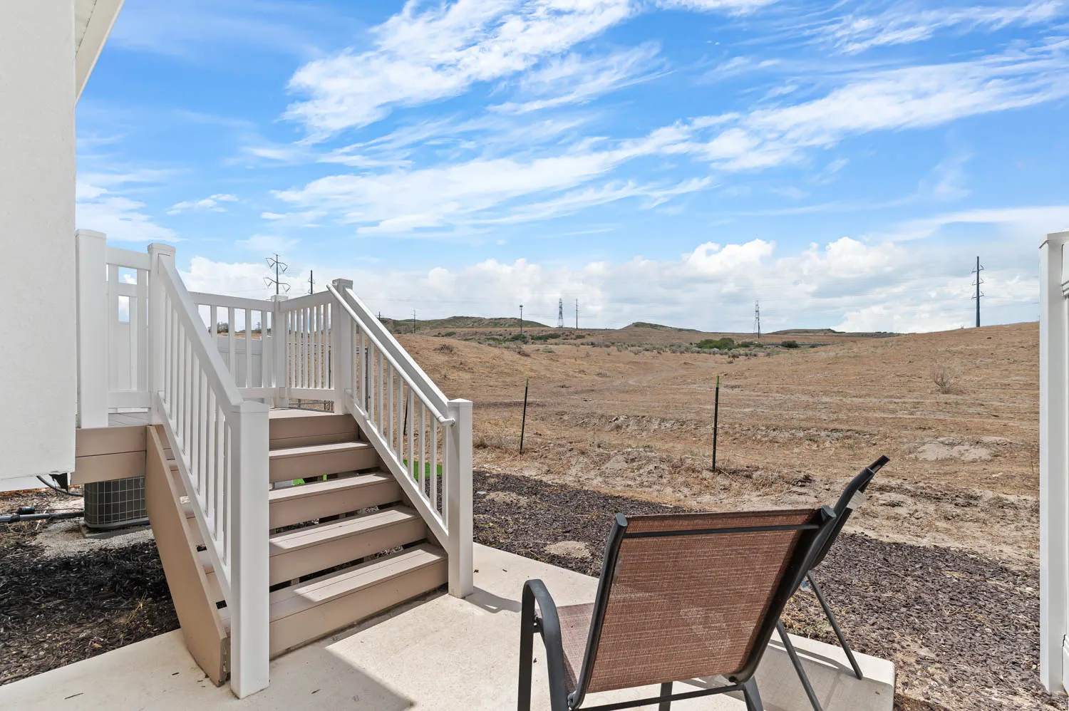 Outdoor patio with concrete flooring, stairs featuring white railings, and an expansive undeveloped landscape