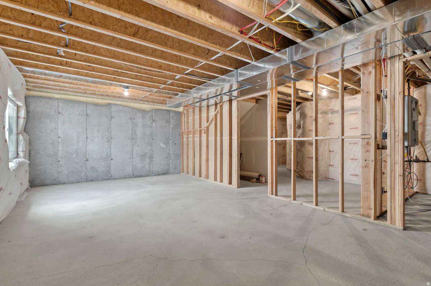 Unfinished basement featuring exposed wood joists, concrete foundation walls, and framed interior walls
