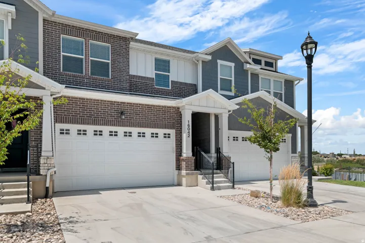 Multi-level residential exterior featuring brick and shingle siding, a two-car garage, covered porch entry, and dedicated driveway space
