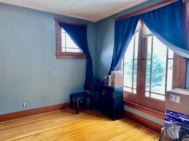 Room with light blue walls, wood-finish flooring, and natural wood trim around windows and glass-paneled doors
