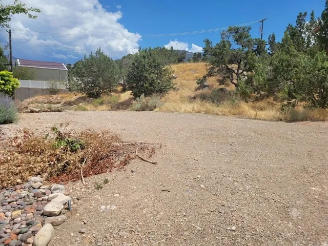 Spacious lot featuring a gravel surface, natural rock landscaping, mature trees, and a sloped terrain