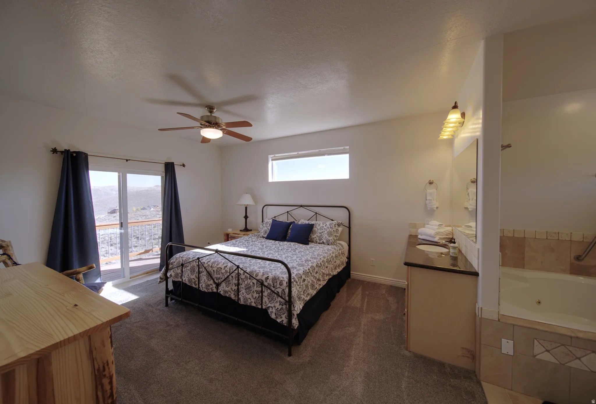 Bedroom featuring direct outdoor access through sliding glass doors, a ceiling fan, and an integrated en-suite bathroom area