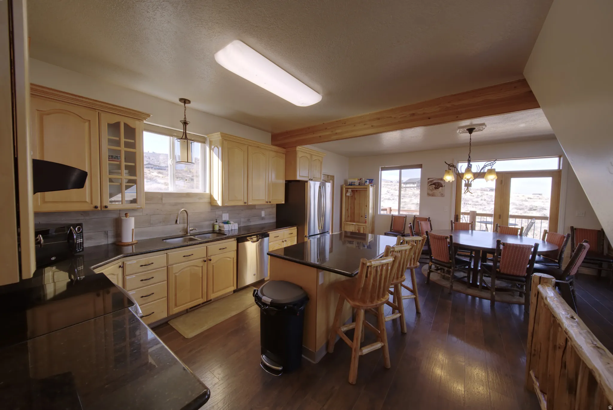 Open-concept kitchen and dining area featuring wood-finish flooring, light wood cabinetry, and dark countertops