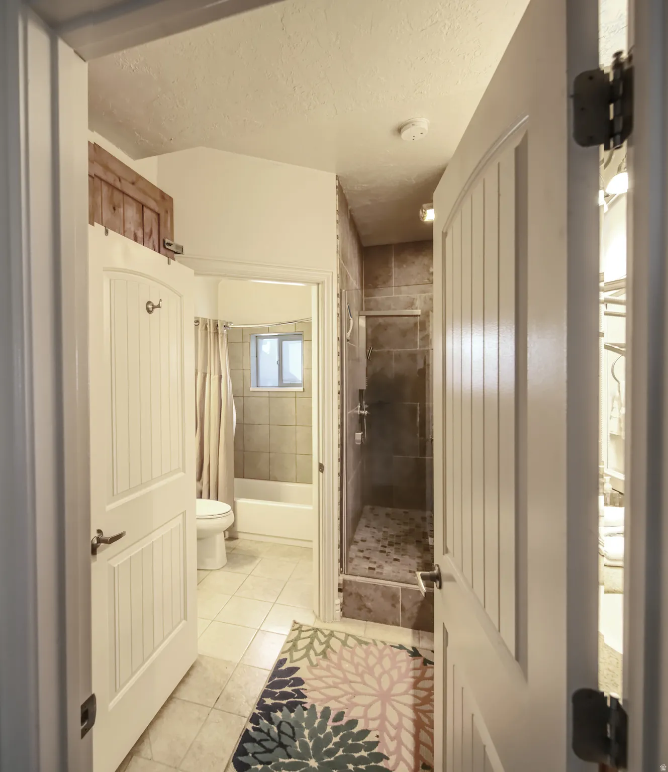 Bathroom featuring a walk-in shower with tile surround and stone-look floor, a separate tub/shower combination with tiled walls, and light-colored tile flooring