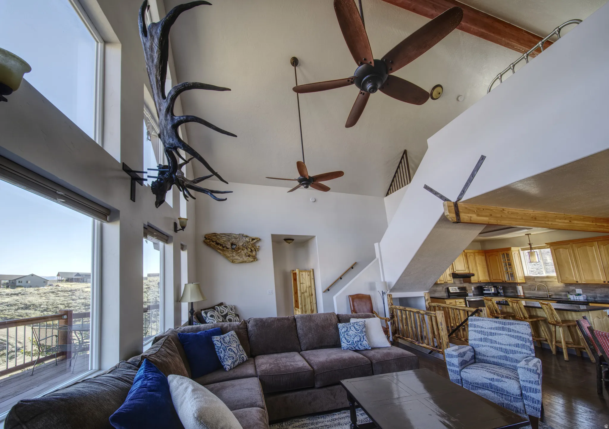 Great room featuring a vaulted ceiling with exposed wood beams, multiple ceiling fans, and large picture windows